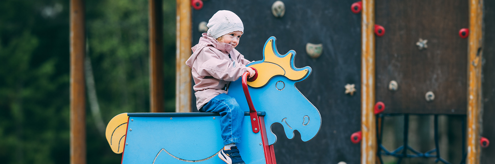 Un niño pequeño se mece en un balancín de juguete con forma de caballo en un parque infantil.